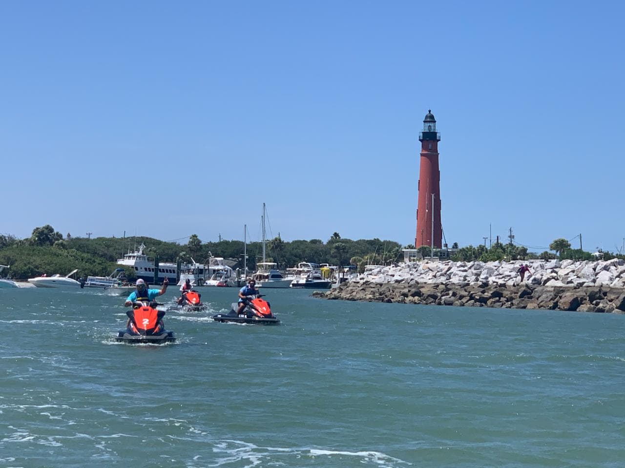 Three Yamaha WaveRunners running in a line past the jetty, the Ponce Inlet Lighthouse behind them.